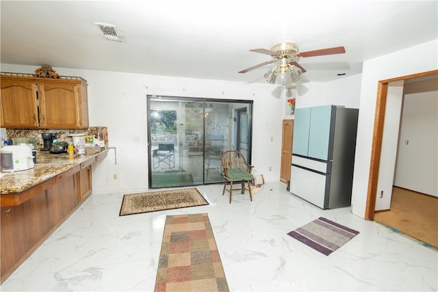 kitchen featuring light stone counters, ceiling fan, tasteful backsplash, and stainless steel fridge