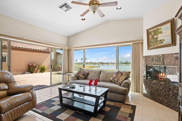 living room featuring ceiling fan, lofted ceiling, a tiled fireplace, a water view, and light tile patterned floors