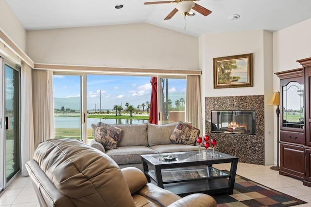 tiled living room with a water view, ceiling fan, a tile fireplace, and lofted ceiling