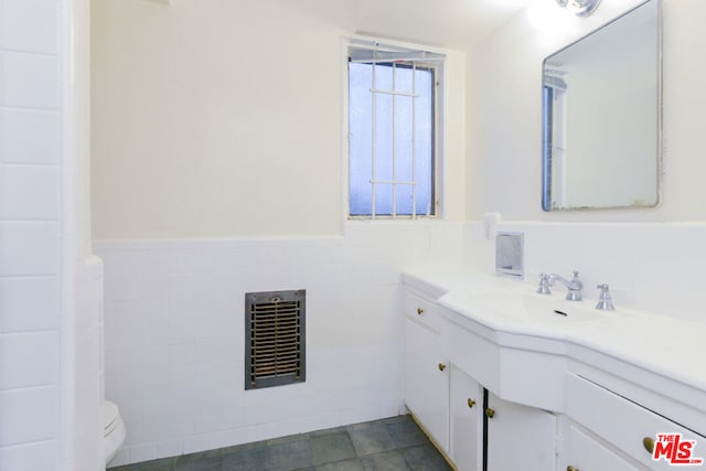 bathroom featuring vanity, heating unit, toilet, and tile walls