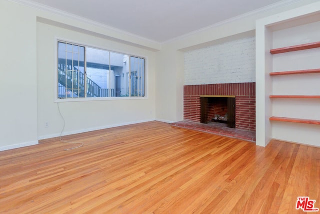 unfurnished living room featuring built in shelves, wood-type flooring, ornamental molding, and a brick fireplace