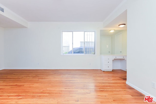 empty room featuring built in desk, ornamental molding, and light hardwood / wood-style flooring