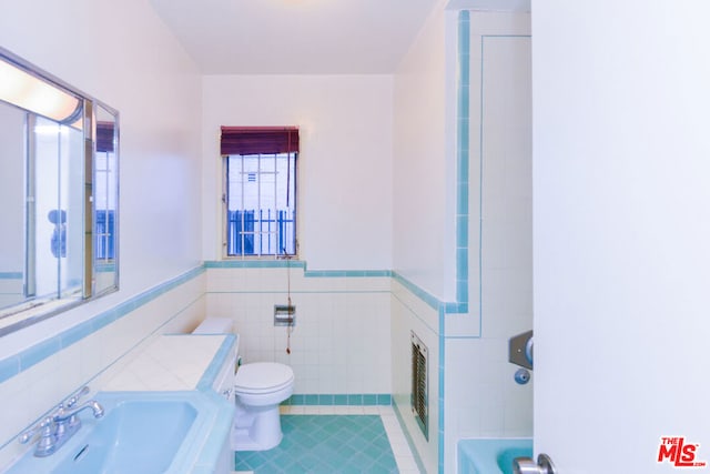 bathroom with heating unit, toilet, sink, and tile walls