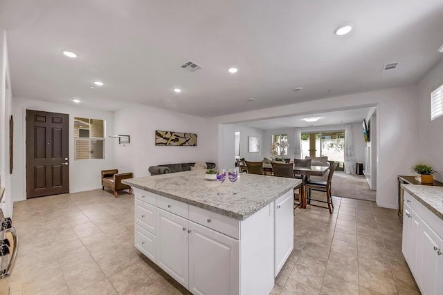 kitchen featuring light stone countertops, a kitchen island, white cabinetry, and light tile patterned floors