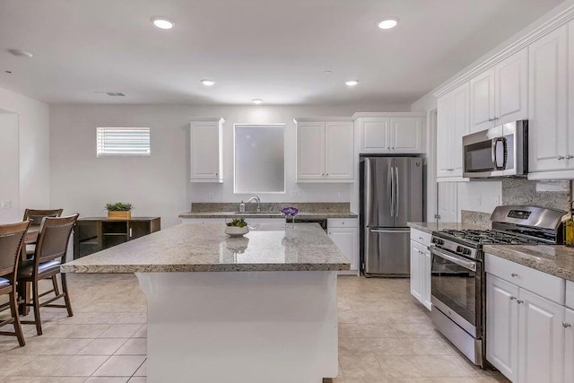 kitchen featuring white cabinets, light stone counters, a kitchen breakfast bar, stainless steel appliances, and a center island