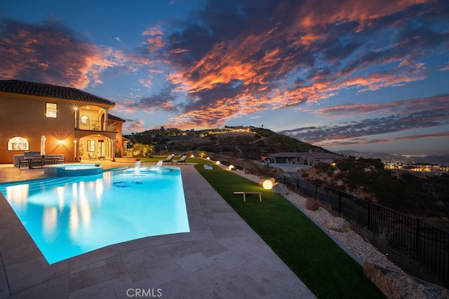 pool at dusk featuring a patio and an in ground hot tub