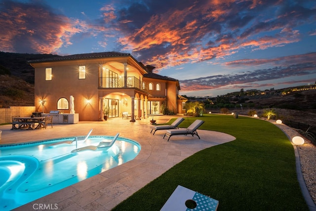 pool at dusk with a patio, a lawn, and a jacuzzi