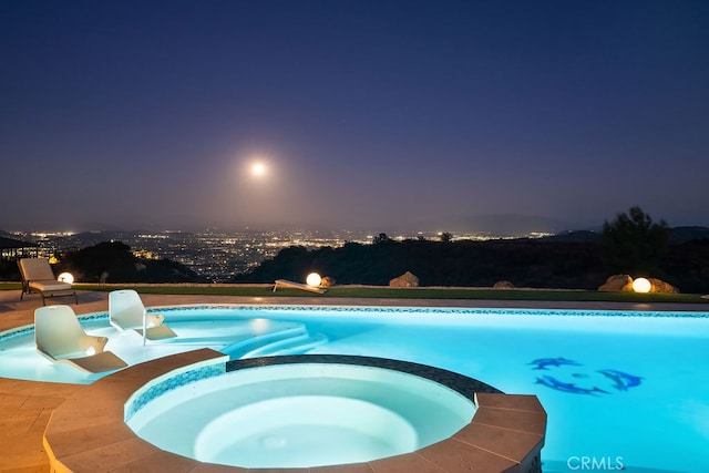 pool at twilight featuring a patio and an in ground hot tub