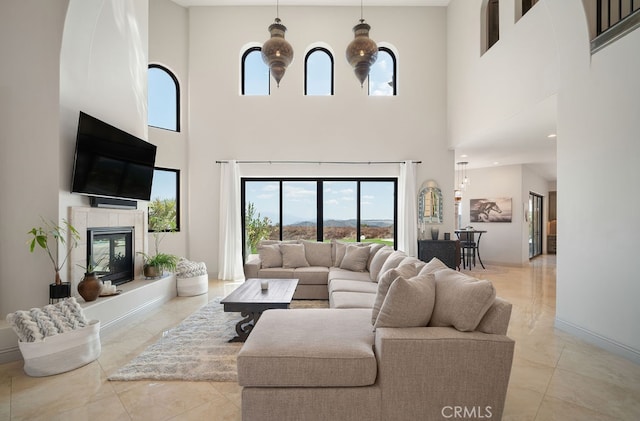 living room featuring a notable chandelier, a tiled fireplace, a high ceiling, and light tile patterned flooring