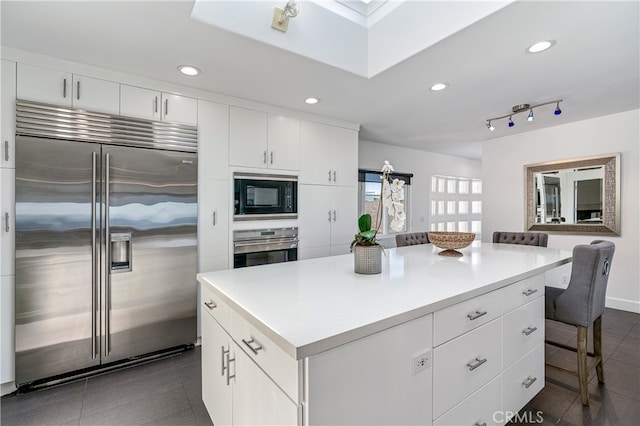 kitchen featuring a kitchen breakfast bar, white cabinetry, a center island, and built in appliances