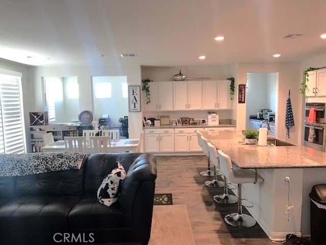 kitchen featuring light stone countertops, sink, double oven, white cabinets, and light wood-type flooring