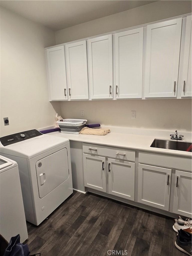 clothes washing area with washing machine and clothes dryer, dark hardwood / wood-style flooring, sink, and cabinets