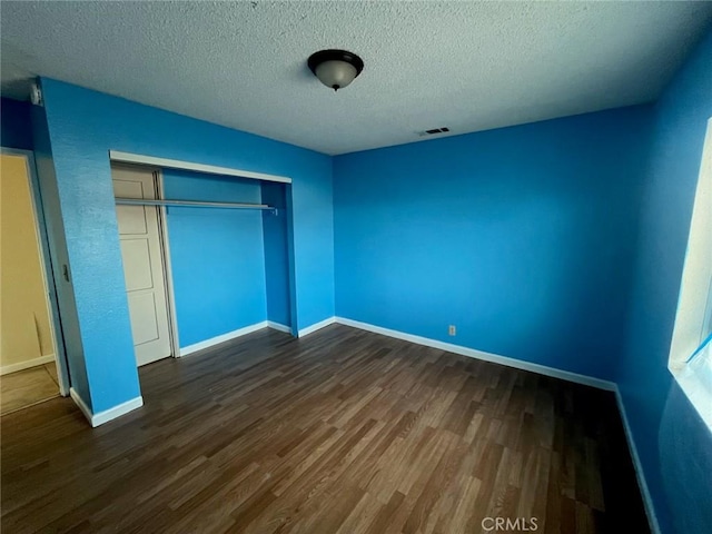 unfurnished bedroom featuring dark hardwood / wood-style floors, a textured ceiling, and a closet