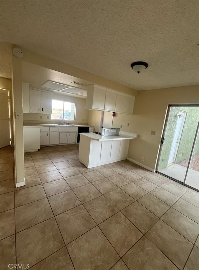 kitchen featuring sink, kitchen peninsula, light tile patterned floors, a textured ceiling, and white cabinetry