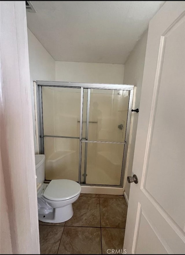 bathroom featuring tile patterned flooring, toilet, and a shower with door