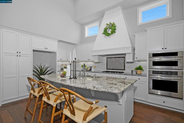 kitchen with white cabinets, a high ceiling, custom range hood, and a breakfast bar area