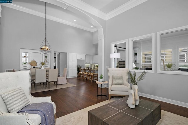 living room with a towering ceiling, dark hardwood / wood-style floors, crown molding, and a notable chandelier