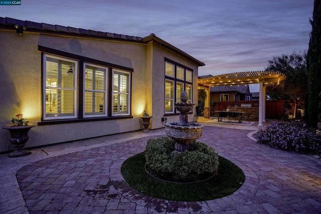 back house at dusk with a pergola and a patio area