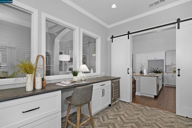 kitchen featuring a kitchen bar, ornamental molding, beverage cooler, a barn door, and white cabinets