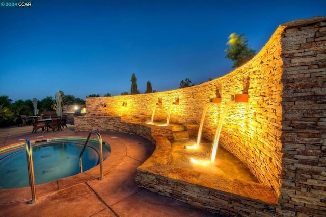 pool at dusk with an in ground hot tub and a patio area