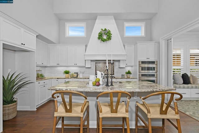 kitchen featuring backsplash, an island with sink, double oven, and custom exhaust hood