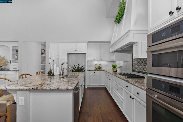 kitchen featuring a center island with sink, light stone countertops, appliances with stainless steel finishes, white cabinetry, and a breakfast bar area