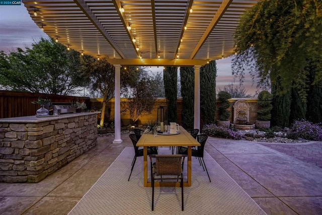 patio terrace at dusk featuring a pergola and an outdoor kitchen