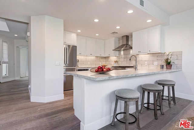 kitchen with white cabinets, sink, high end fridge, wall chimney exhaust hood, and dark wood-type flooring