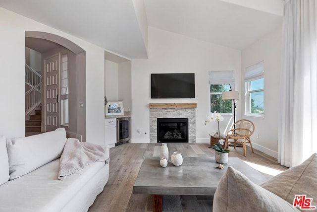 living room featuring light wood-type flooring, lofted ceiling, a fireplace, and wine cooler