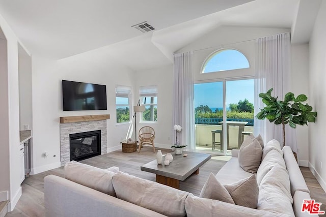 living room featuring vaulted ceiling, light hardwood / wood-style floors, and a stone fireplace