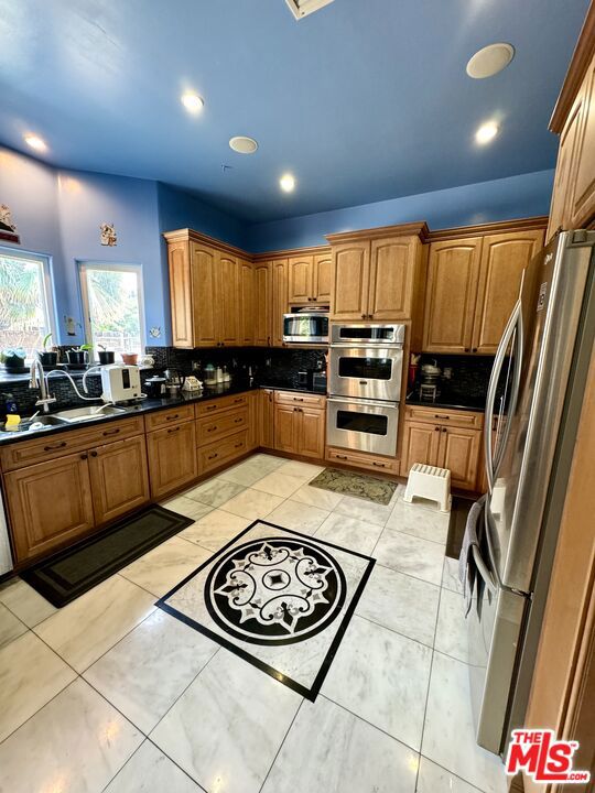 kitchen with dark stone countertops, light tile patterned floors, stainless steel appliances, and tasteful backsplash