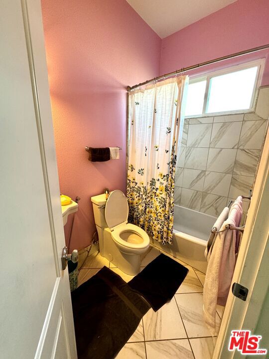 bathroom featuring shower / bath combination with curtain, tile patterned flooring, and toilet