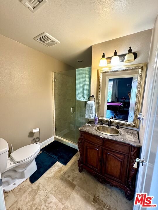 bathroom with a textured ceiling, vanity, toilet, and a shower with shower door