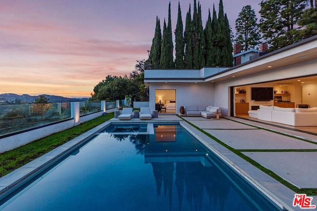 pool at dusk with a patio and outdoor lounge area