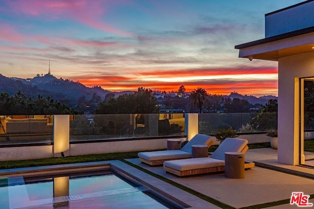 pool at dusk featuring a patio and a mountain view