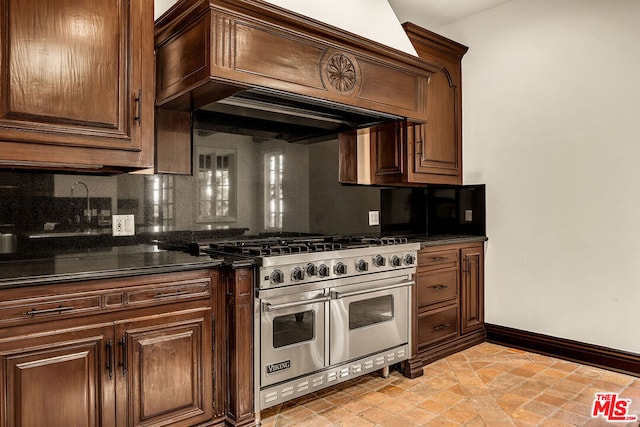 kitchen featuring premium range hood, dark stone counters, backsplash, and double oven range