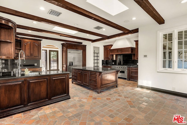 kitchen featuring custom range hood, backsplash, a skylight, high quality appliances, and a kitchen island with sink