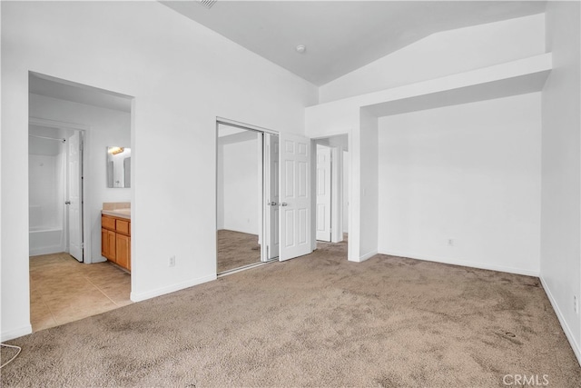 unfurnished bedroom featuring connected bathroom, vaulted ceiling, light carpet, and a closet