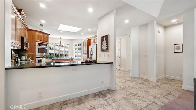 kitchen with a skylight, sink, stainless steel appliances, hanging light fixtures, and kitchen peninsula