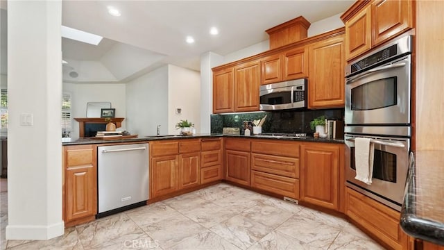 kitchen featuring kitchen peninsula, backsplash, dark stone counters, stainless steel appliances, and sink