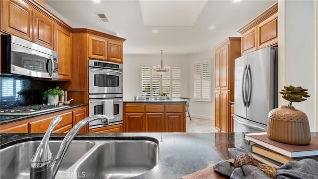 kitchen featuring sink, stainless steel appliances, a notable chandelier, decorative light fixtures, and decorative backsplash