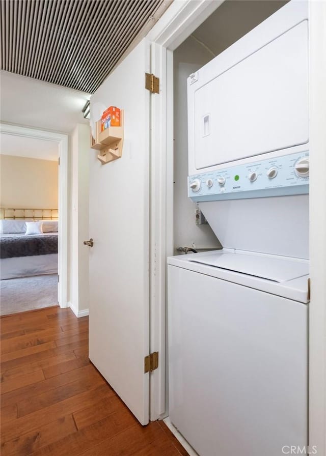 clothes washing area featuring hardwood / wood-style floors and stacked washer and clothes dryer