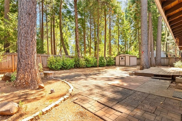 view of patio with a storage shed, a fenced backyard, a wooden deck, and an outbuilding