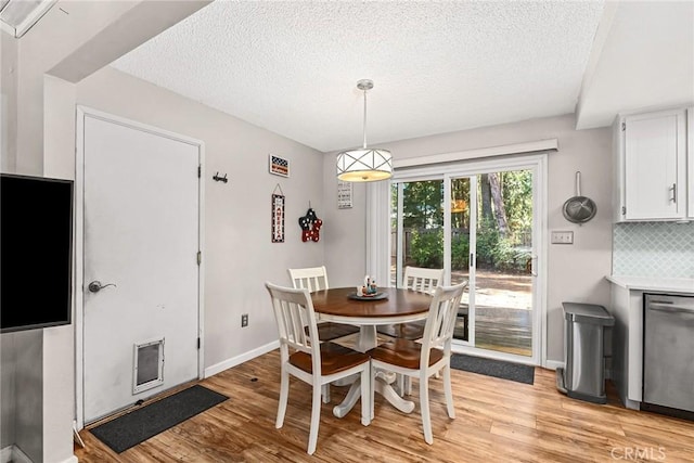 dining space featuring light wood-style flooring, baseboards, and a textured ceiling