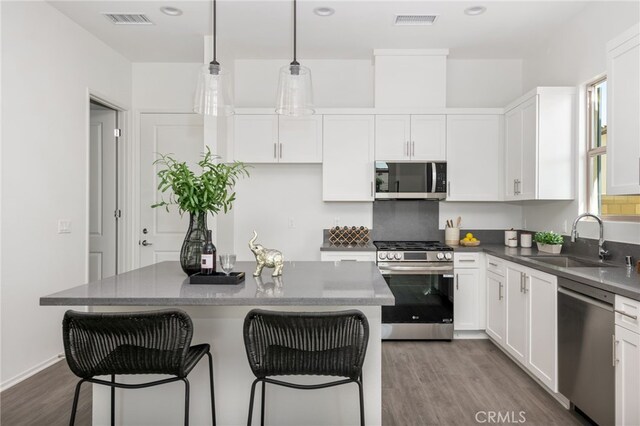 kitchen featuring appliances with stainless steel finishes, hardwood / wood-style floors, pendant lighting, white cabinetry, and sink