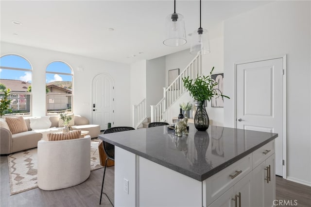 kitchen featuring dark wood-type flooring, white cabinetry, hanging light fixtures, dark stone countertops, and a kitchen breakfast bar