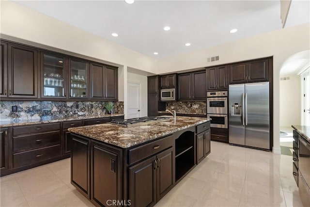 kitchen with stainless steel appliances, tasteful backsplash, dark brown cabinetry, and a kitchen island with sink