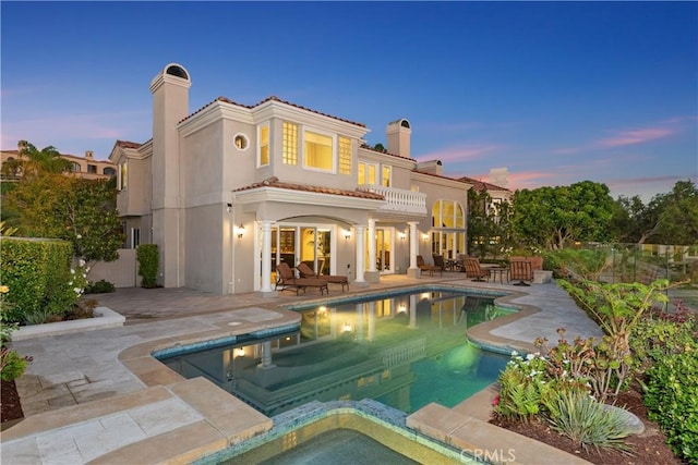 back of property at dusk featuring a balcony, a tile roof, stucco siding, a chimney, and a patio area