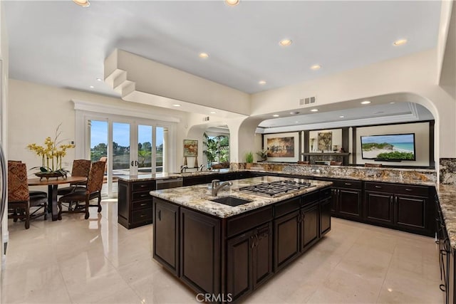 kitchen with an island with sink, sink, kitchen peninsula, light stone counters, and stainless steel gas stovetop