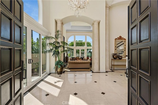 foyer entrance featuring ornate columns, a healthy amount of sunlight, a towering ceiling, and a notable chandelier